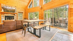 Ein rustikales Blockhaus-Interieur mit Kamin, Essbereich und großen Fenstern mit Blick auf den Wald.