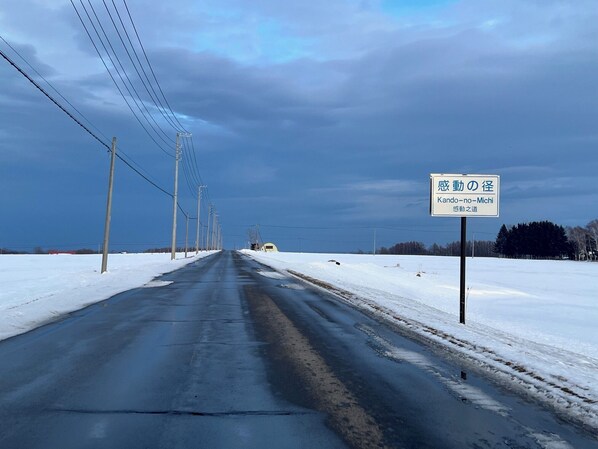 A road with a snow-covered landscape, utility poles, and a road sign indicating direction. - Cottage Abashiri (Abashiri)