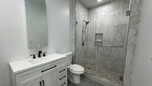 Un baño moderno con tocador blanco, inodoro y zona de ducha con mampara y azulejos de mármol.