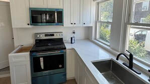 Cocina moderna con armarios blancos, estufa negra, microondas y un amplio ventanal con vistas al exterior.