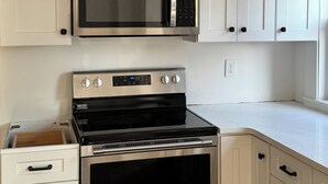 Una cocina con gabinetes blancos, un microondas de acero inoxidable y una estufa negra.