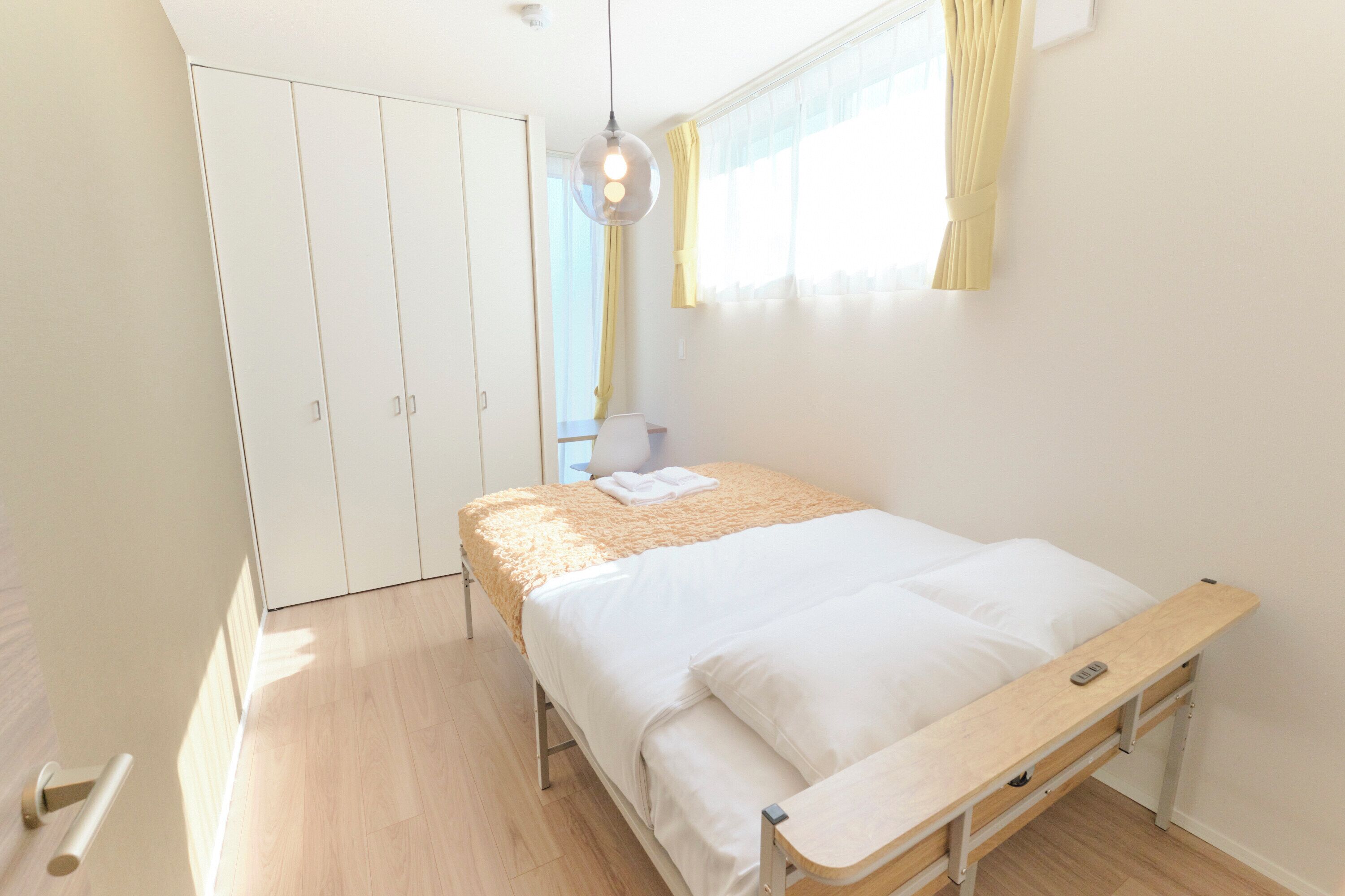 A bedroom with a bed, a bedside table, a wardrobe, and a window with curtains.