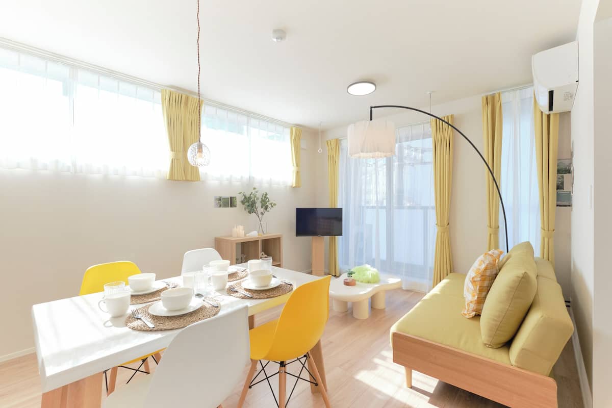 Una sala de estar moderna con comedor, sillas amarillas, un sofá y una televisión.