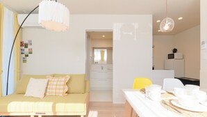 A modern living room with a sofa, dining table set with white dishes, and a kitchen in the background. - Everynet Shinjuku II by Tranova (Tokyo)