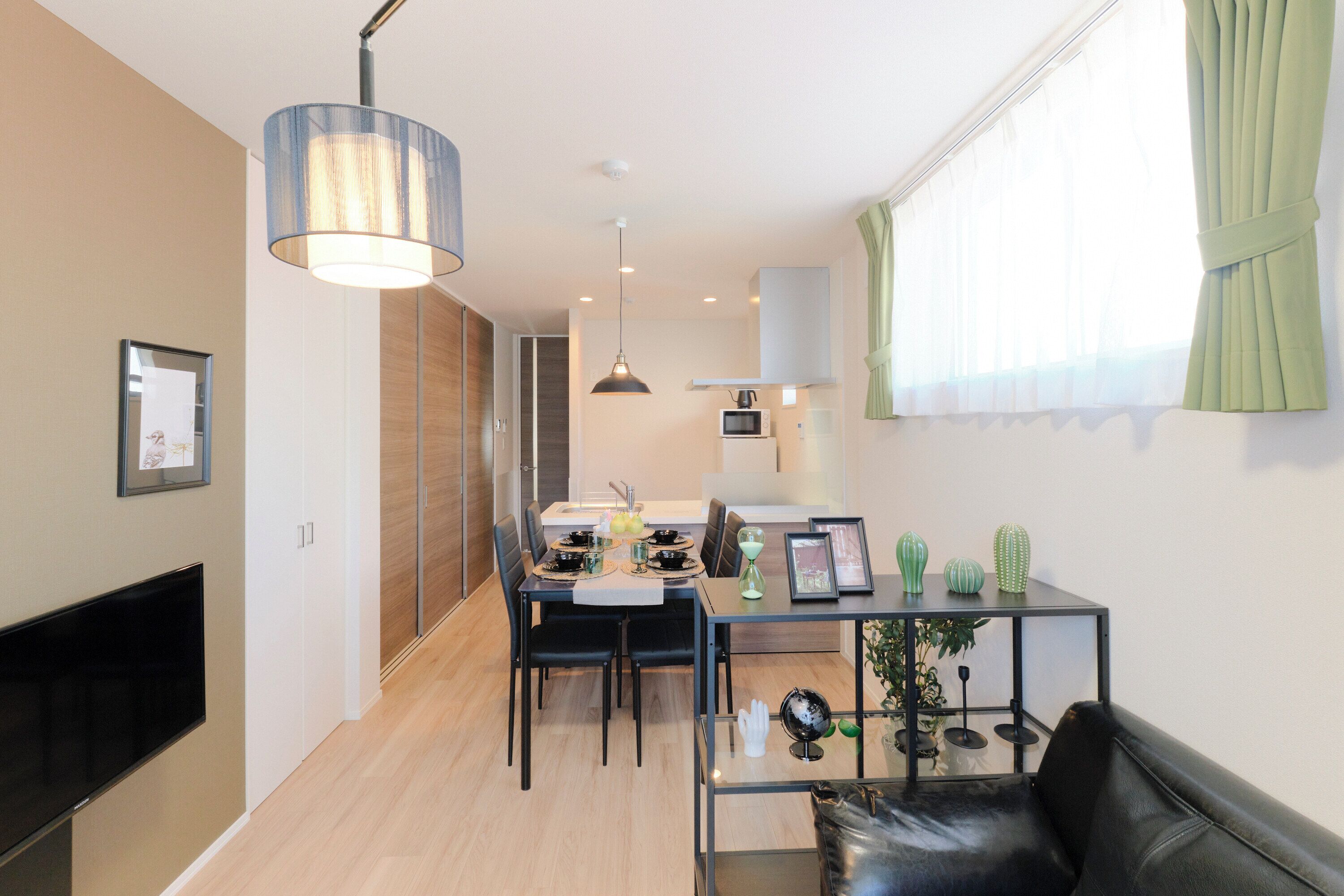 A modern living room with a black leather sofa, a glass coffee table, and a dining area with a table set for two.