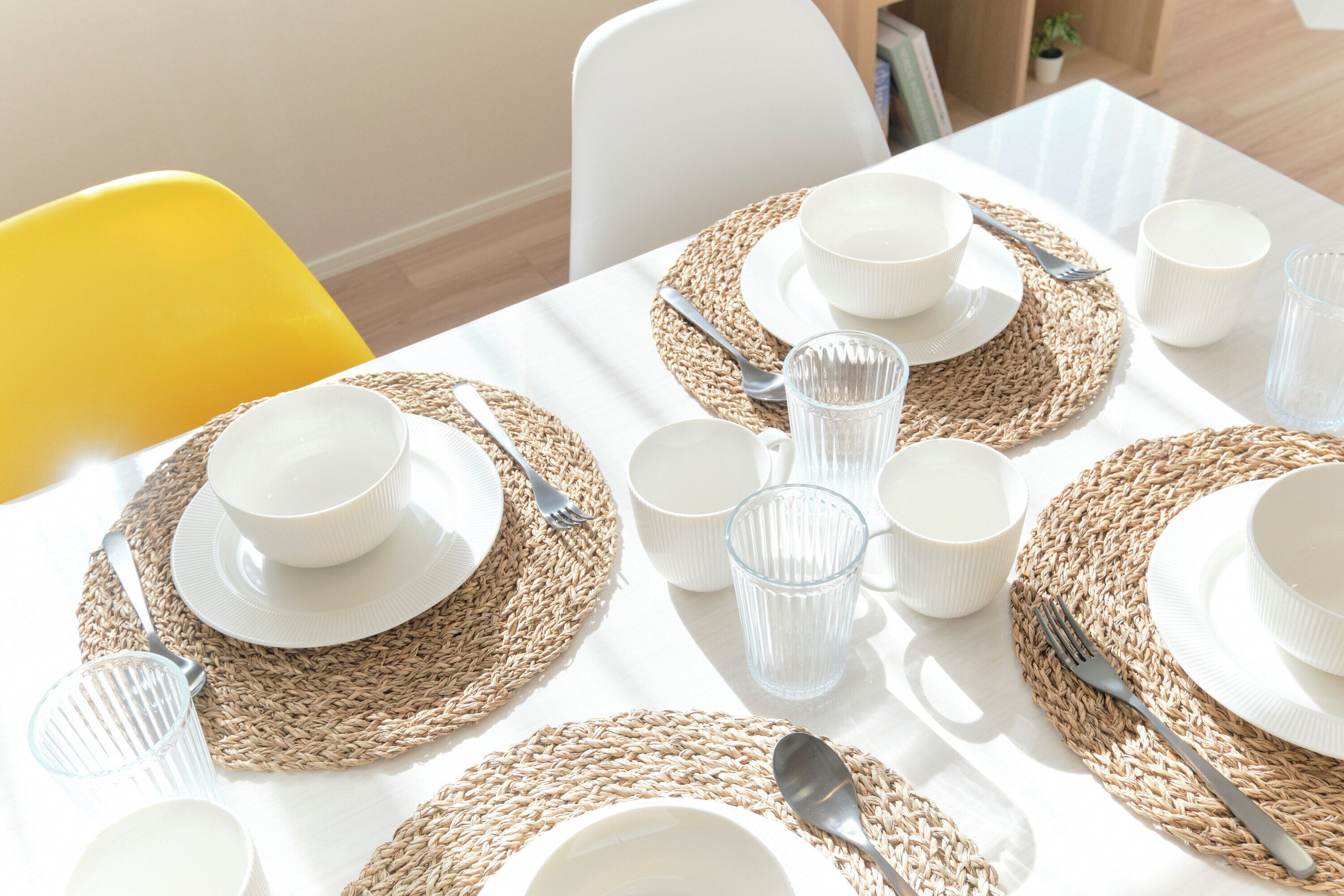 Una mesa dispuesta con platos, tazones y cubiertos blancos, sobre un mantel blanco con individuales tejidos.