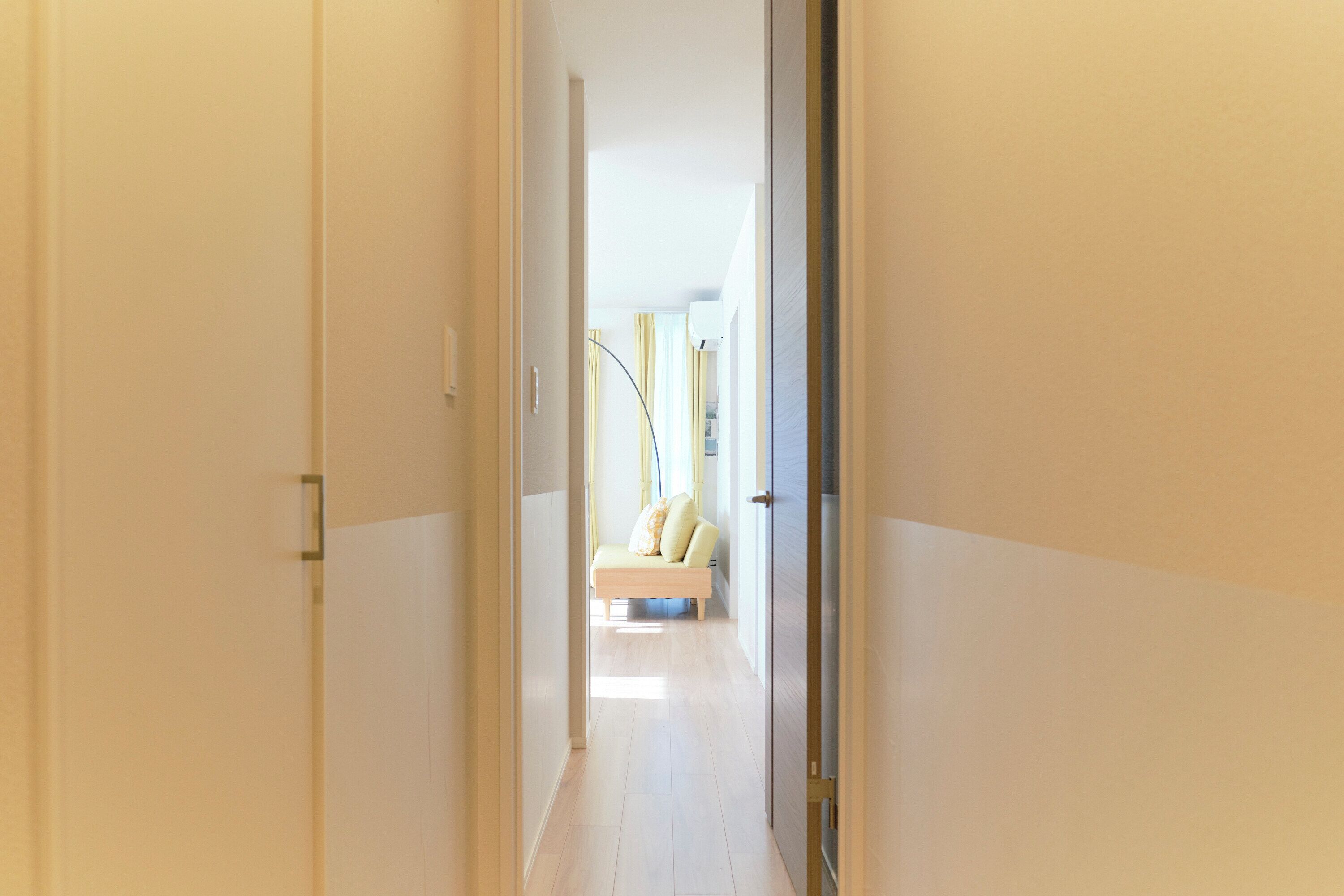 A narrow hallway with a bench in the distance, leading to a room with a bed and curtains.