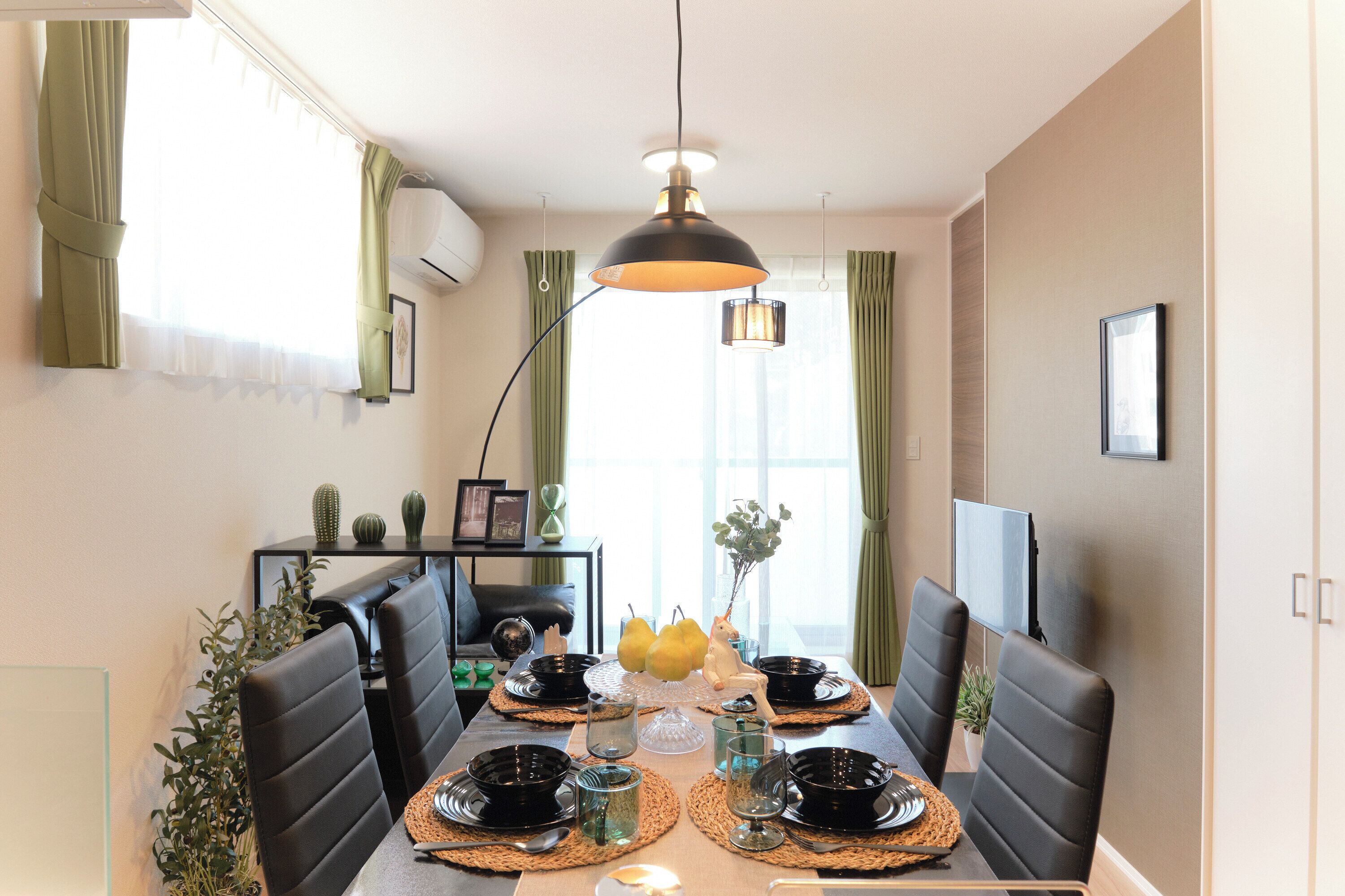 A dining area with a table set for four, black chairs, a central light fixture, and a television on the wall.