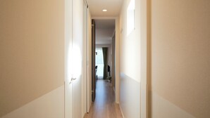 A narrow hallway with a door on the left, a window on the right, and a plant in the center. - Everynet Shinjuku II by Tranova (Tokyo)