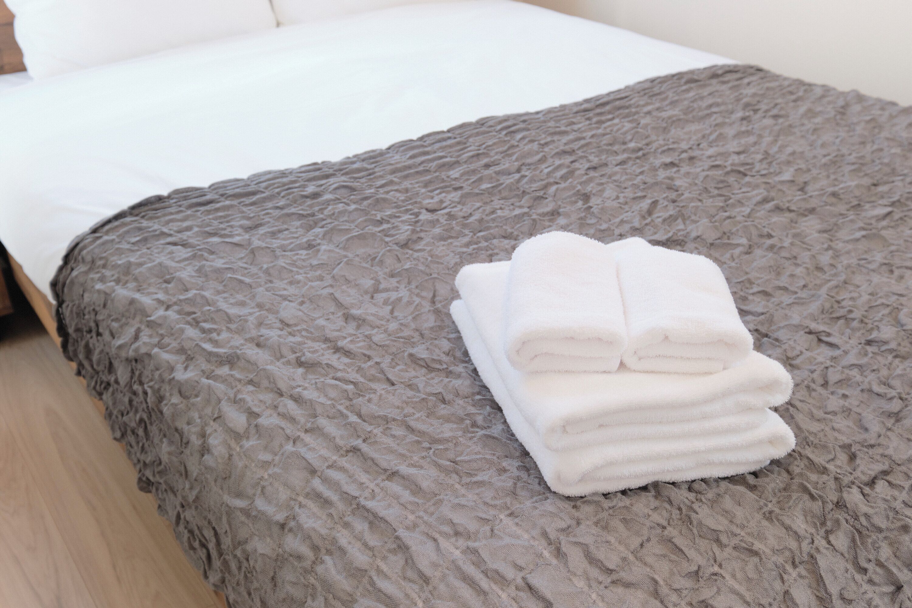 Un lit bien fait, recouvert d’une couverture grise à texture et agrémenté d’une pile de serviettes blanches.