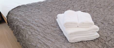 Un lit bien fait, recouvert d’une couverture grise à texture et agrémenté d’une pile de serviettes blanches.