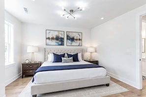Quarto com uma cama grande, duas mesas de cabeceira, um candelabro e duas pinturas abstratas na parede.