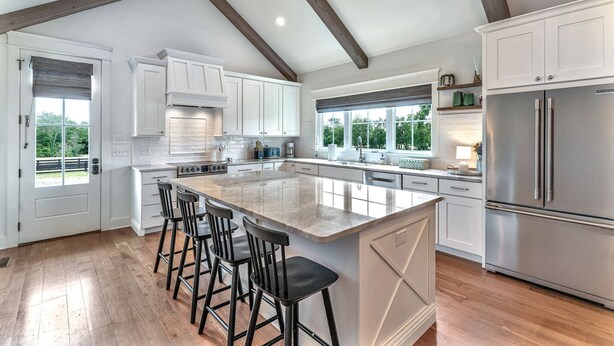 A spacious kitchen with white cabinetry, a large island with bar stools, and a stainless steel refrigerator. - 32 Acre Farm at Maven Stables ｜Spring Hill (Columbia)