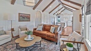 A spacious living room with a brown leather sofa, a coffee table, and a dining area with a chandelier. - 32 Acre Farm at Maven Stables ｜Spring Hill (Columbia)