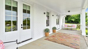 A covered porch with a white brick exterior, a concrete floor, and a colorful rug. - 32 Acre Farm at Maven Stables ｜Spring Hill (Columbia)