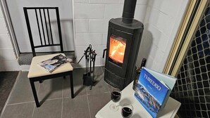 Ett rum med en svart vedkamin, en stol, ett bord med en bok och två glas rött vin.