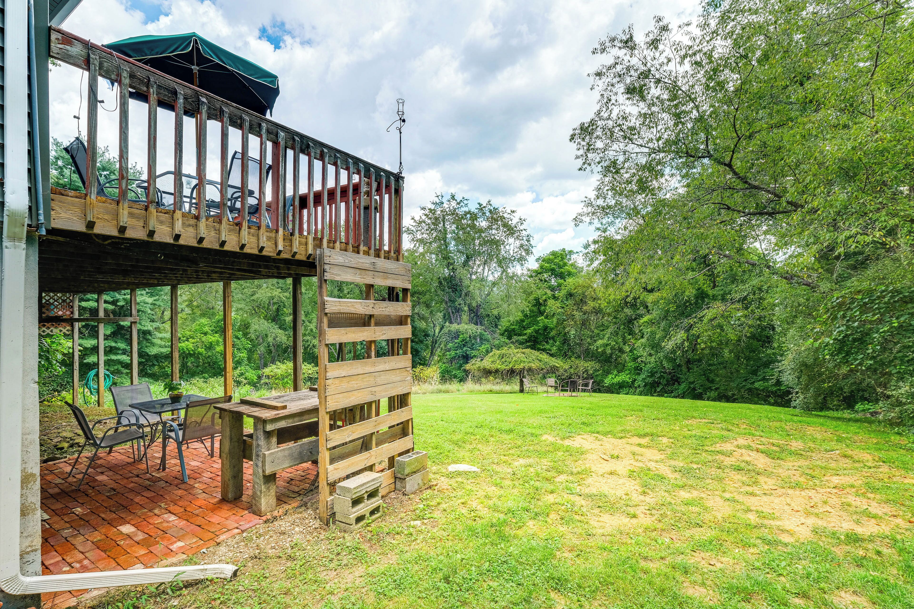 A wooden deck with a table and chairs, a covered area with chairs, and a view of a grassy area with trees.