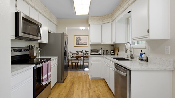 Una cucina moderna con mobili bianchi, forno a microonde, piano cottura e lavastoviglie.