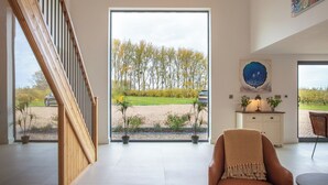 A spacious living room with a large window, a staircase, and a view of a garden. - Orchard Barn-Luxury 4 BD Barn Conversion (Pershore)