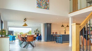 A spacious living area with a dining table, chairs, and a kitchen area with bar stools. - Orchard Barn-Luxury 4 BD Barn Conversion (Pershore)