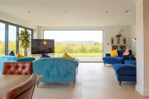 A spacious living room with large windows, a television, and two sofas with colorful cushions. - Orchard Barn-Luxury 4 BD Barn Conversion (Pershore)