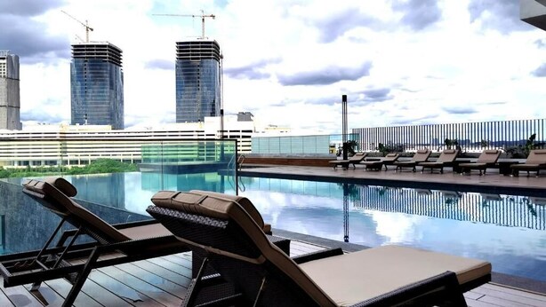 A rooftop pool with lounge chairs, a glass barrier, and modern buildings in the background. - City View Southkey 2BR2FREE 18F By Natol (Johor Bahru)
