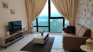 A living room with a TV, sofa, coffee table, and a view of buildings through large windows. - City View Southkey 2BR2FREE 18F By Natol (Johor Bahru)
