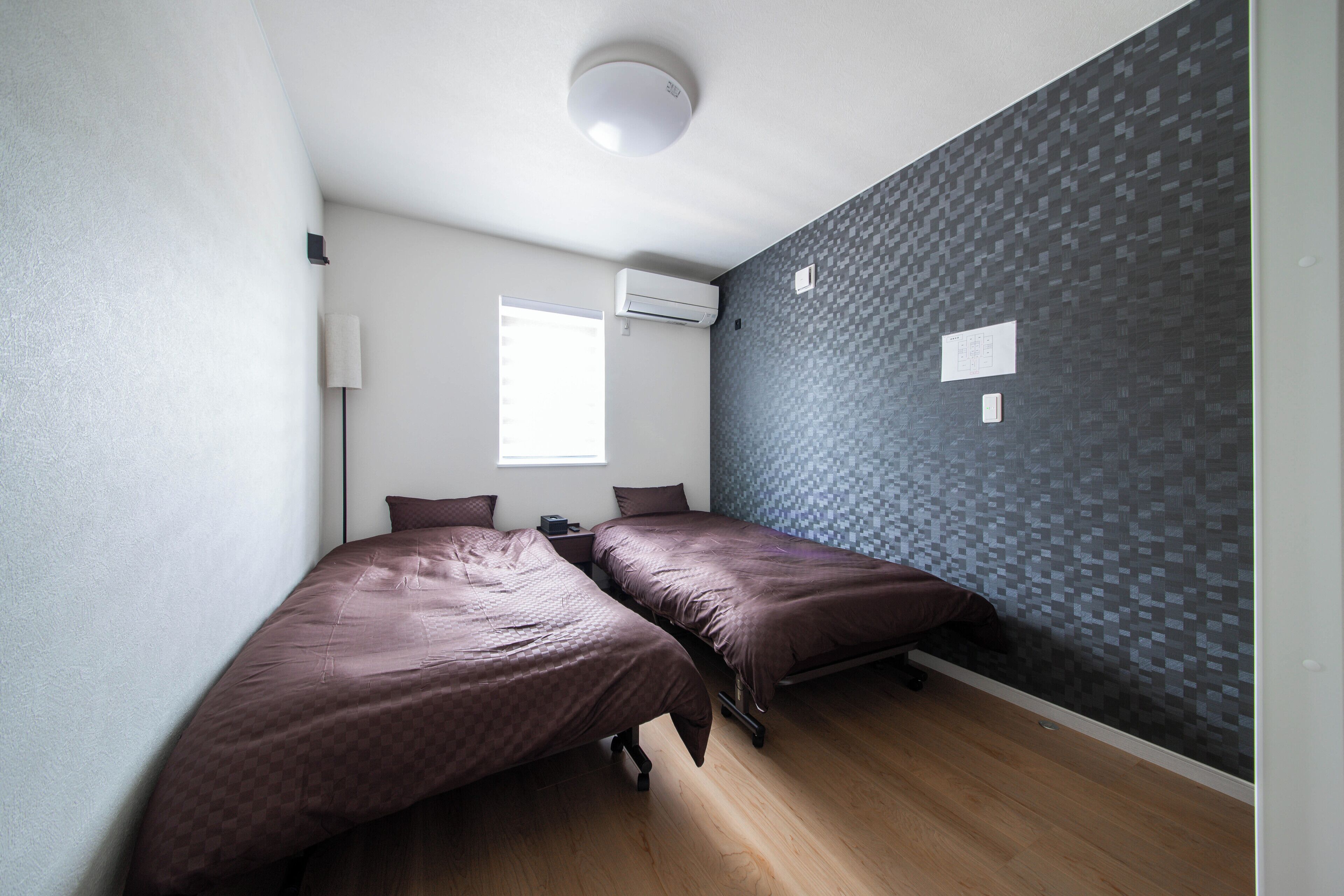 A room with two beds, a window, an air conditioning unit, and a textured wall.