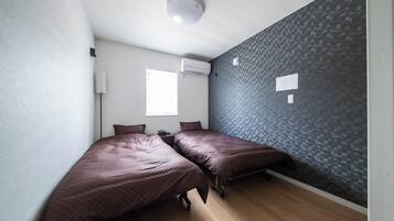 A room with two beds, a window, an air conditioning unit, and a textured wall.