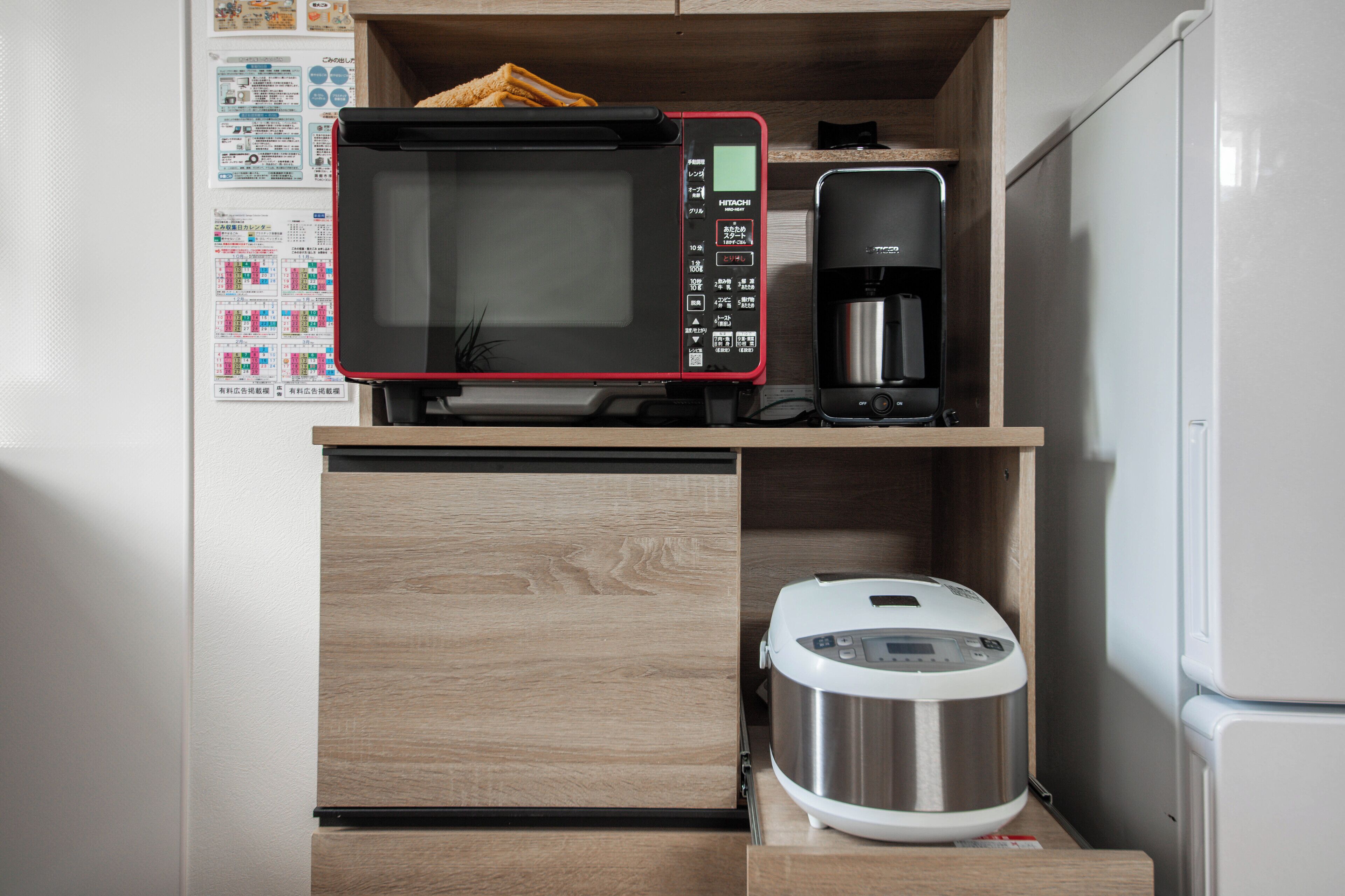 Une petite cuisine équipée d’un four à micro-ondes, d’une machine à café et d’un cuiseur à riz, le tout placé sur une étagère en bois.