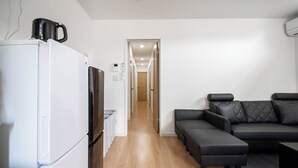 Una sala de estar moderna con un refrigerador blanco, un televisor de pantalla plana, un sofá de cuero oscuro y piso de madera.