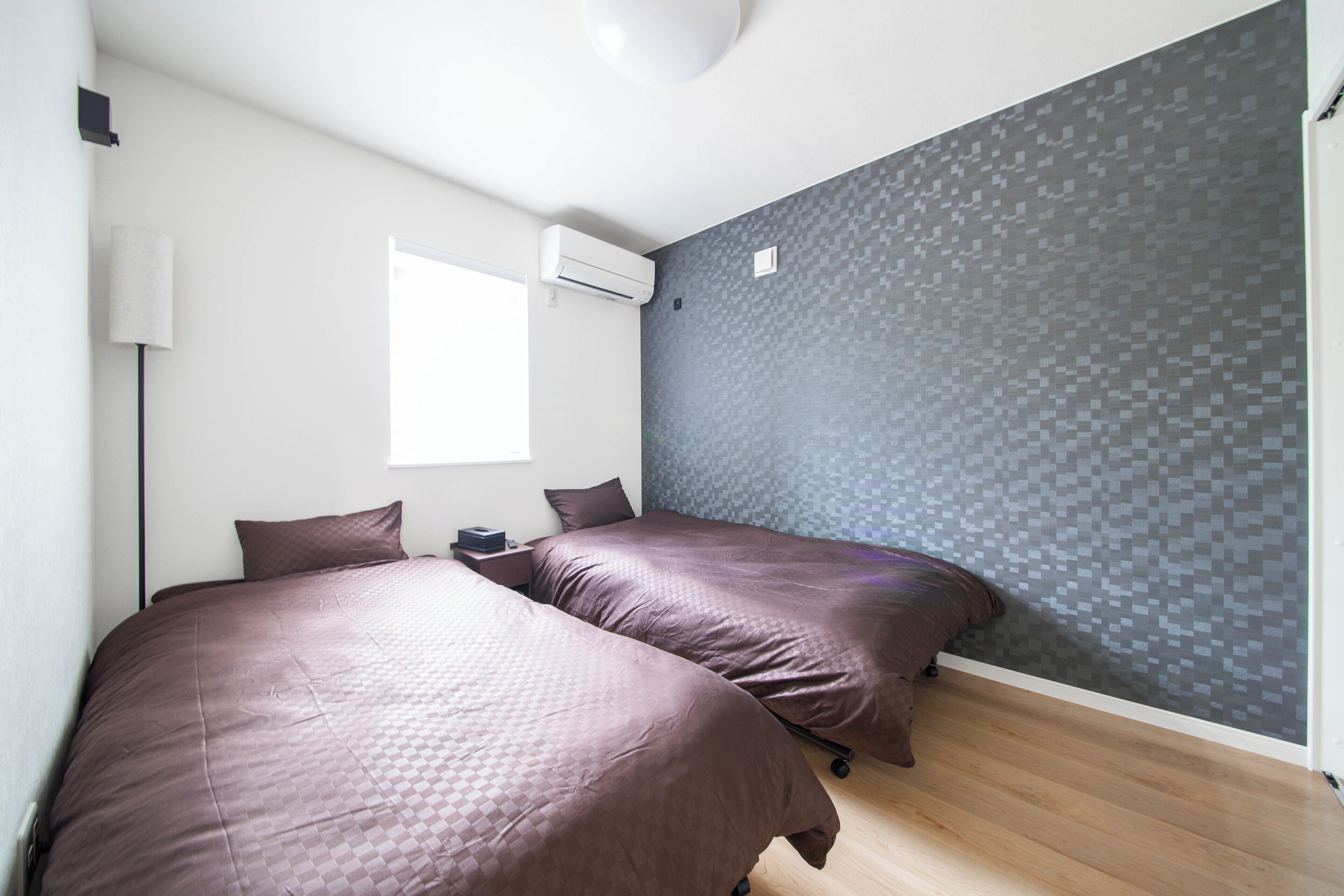A bedroom with two beds, a window, an air conditioning unit, and a textured wall.