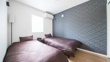 A bedroom with two beds, a window, an air conditioning unit, and a textured wall.