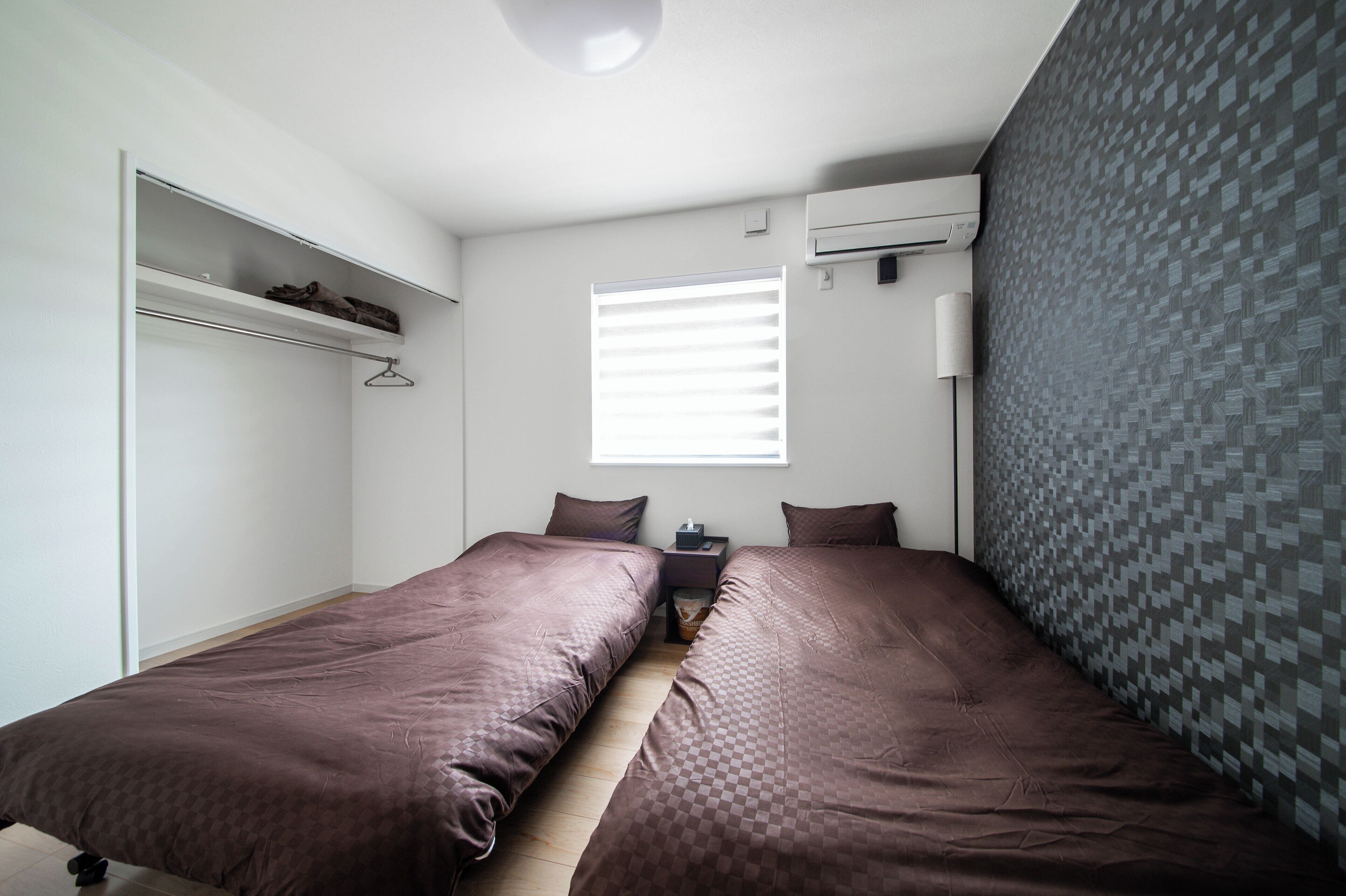 Un dormitorio con dos camas, un armario, una ventana con persianas, un equipo de aire acondicionado y una pared con diseño.