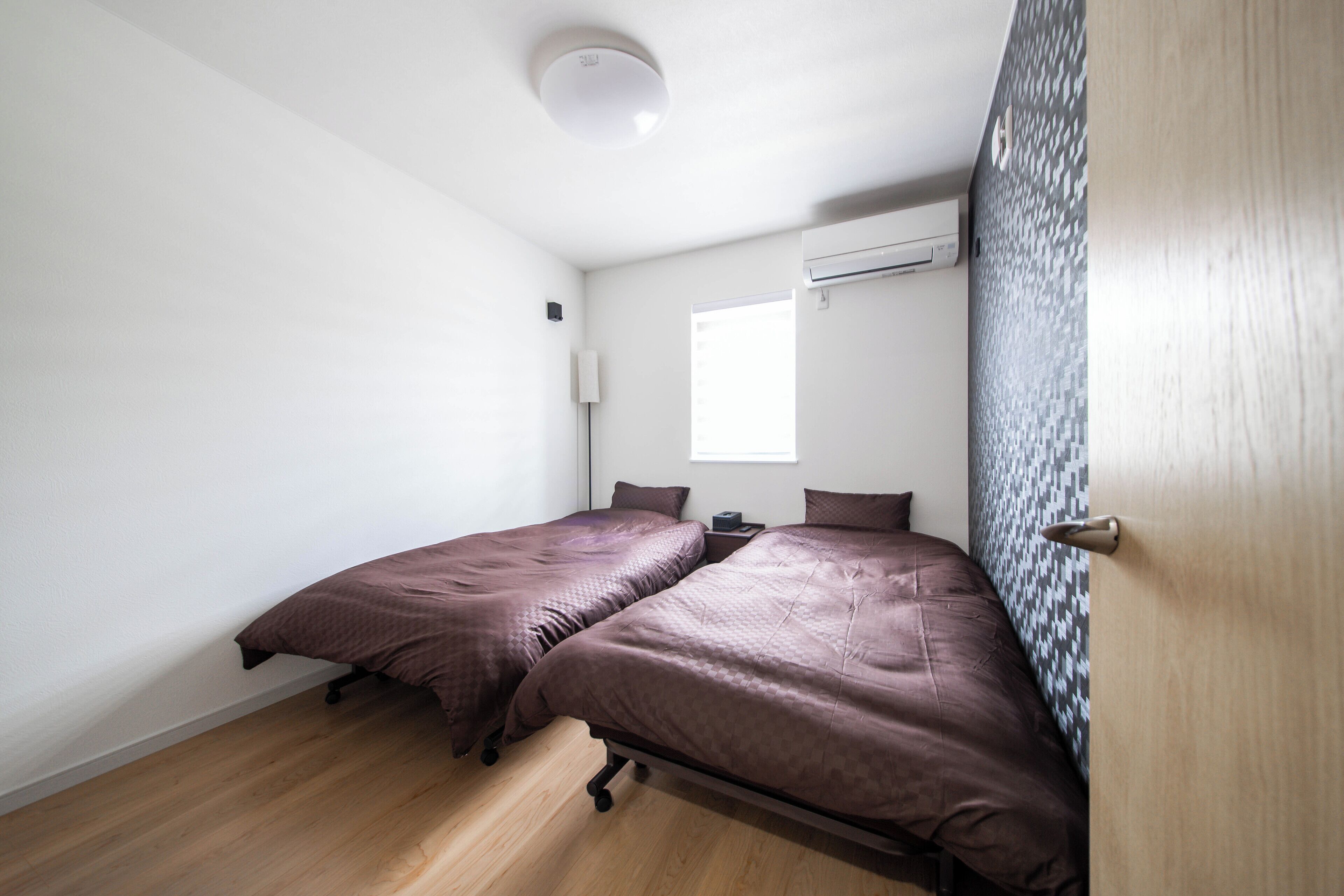 A bedroom with two beds, a window, an air conditioning unit, and a door with a textured panel.