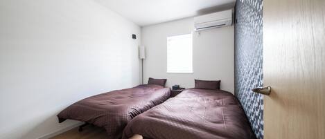 A bedroom with two beds, a window, an air conditioning unit, and a door with a textured panel.