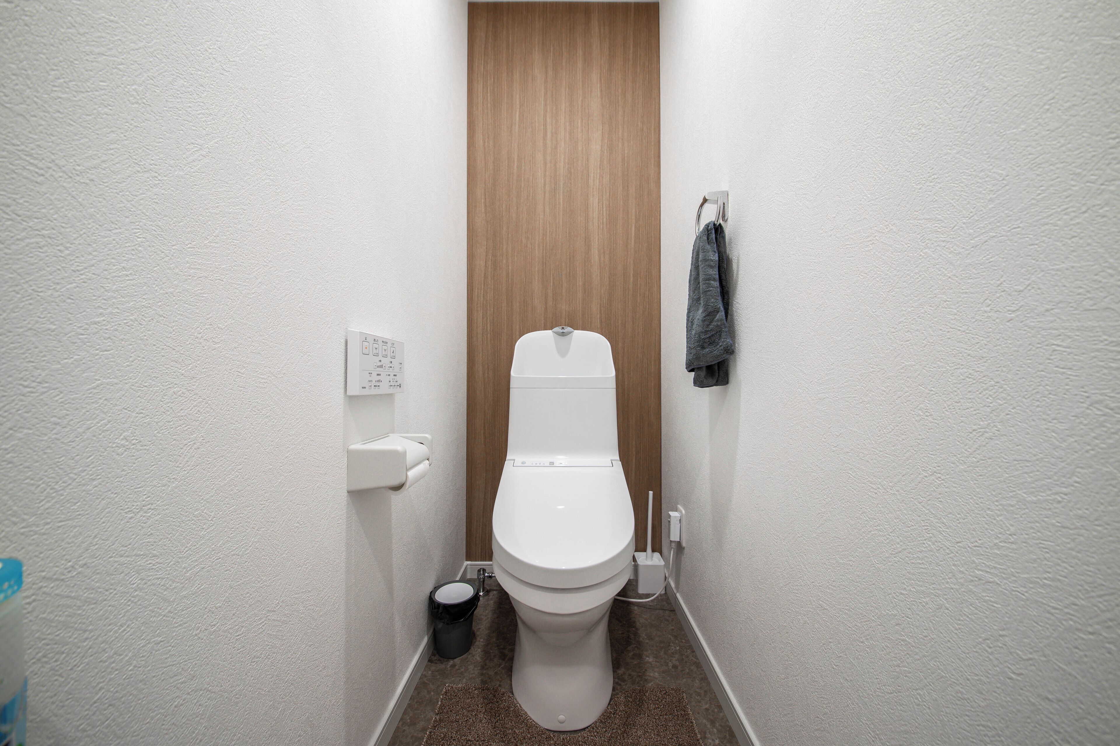 Un baño pequeño y estrecho con un inodoro blanco, una puerta de madera y una toalla colgada en la pared.