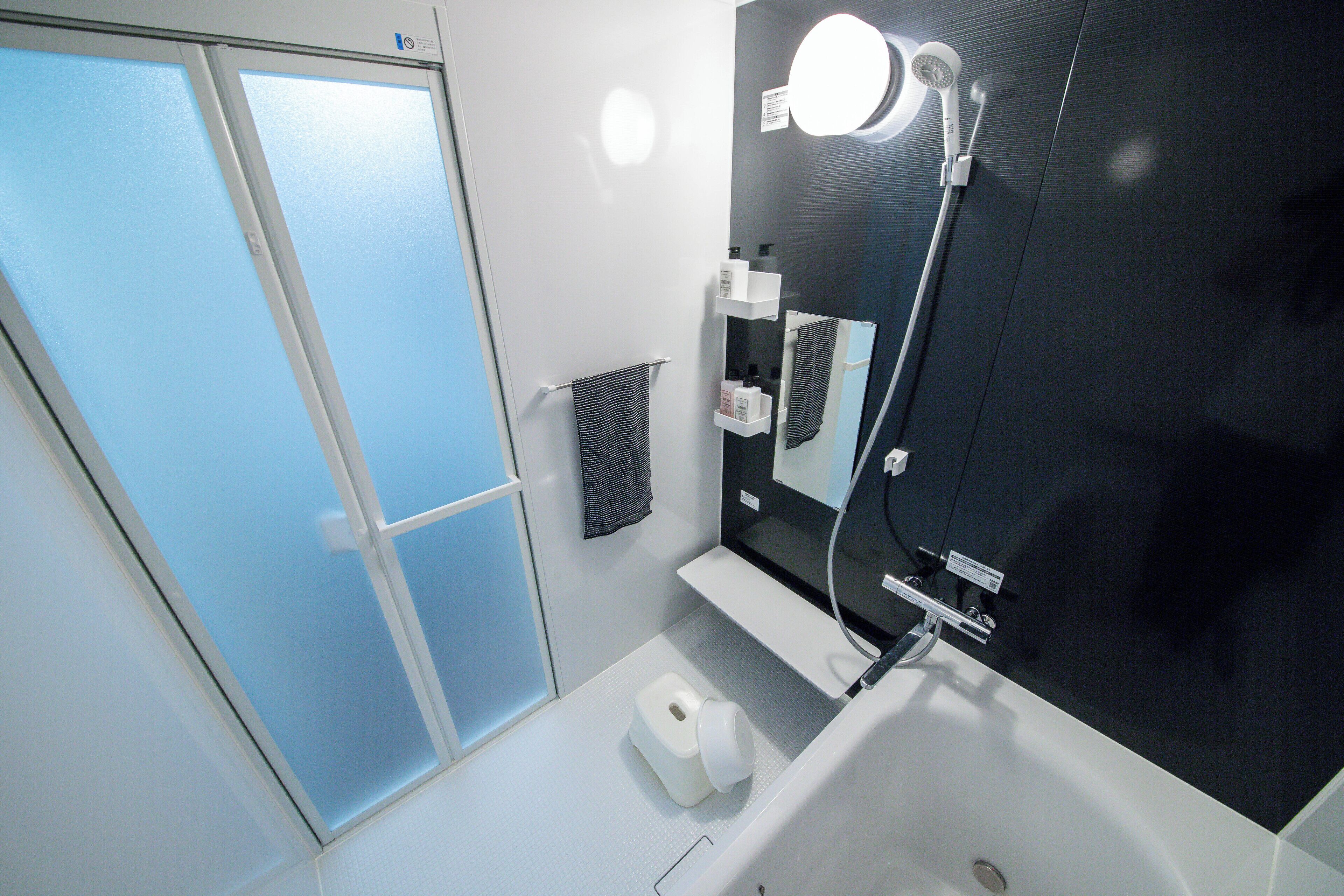 Et moderne badeværelse med et stort spejl, et håndholdt brusehoved og en toiletpapirholder.