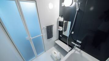 Et moderne badeværelse med et stort spejl, et håndholdt brusehoved og en toiletpapirholder.