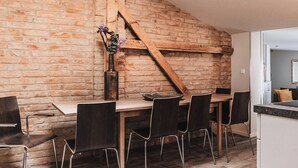 A dining area with a brick wall, wooden beams, and a table with chairs. - Fontane Apartments (Schorfheide)