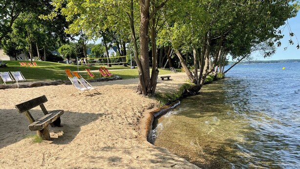 A beach with a wooden bench, clear shallow water, and a grassy area with beach chairs. - Fontane Apartments (Schorfheide)