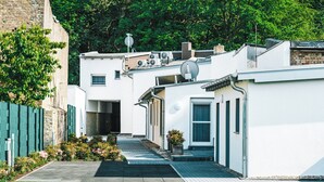 A modern residential building with a clean, white exterior, a paved driveway, and a small garden area with flowers. - Fontane Apartments (Schorfheide)