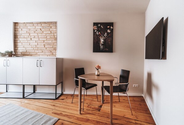 Un espace repas moderne avec une table en bois, deux chaises, un vase de fleurs, un mur en briques et un tableau accroché au mur.