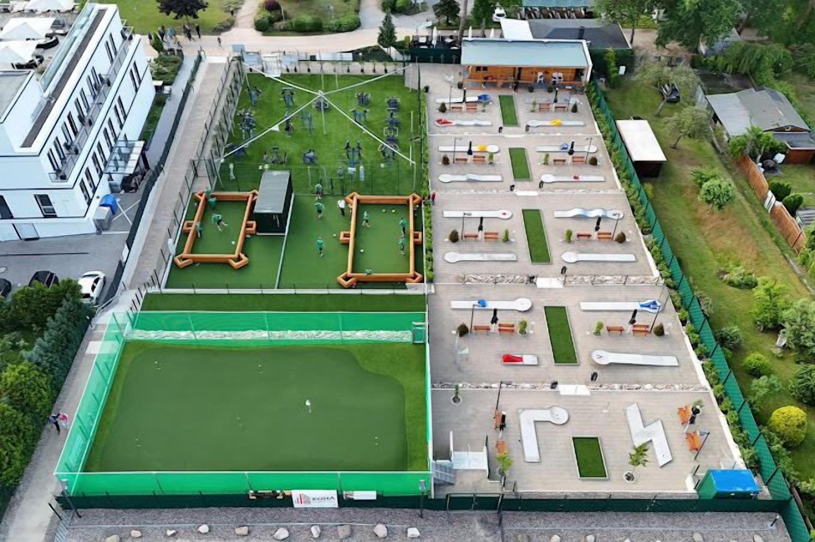 An aerial view of a sports facility with multiple courts, including a large green field and smaller courts with various sports equipment.