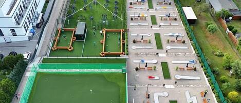 An aerial view of a sports facility with multiple courts, including a large green field and smaller courts with various sports equipment.