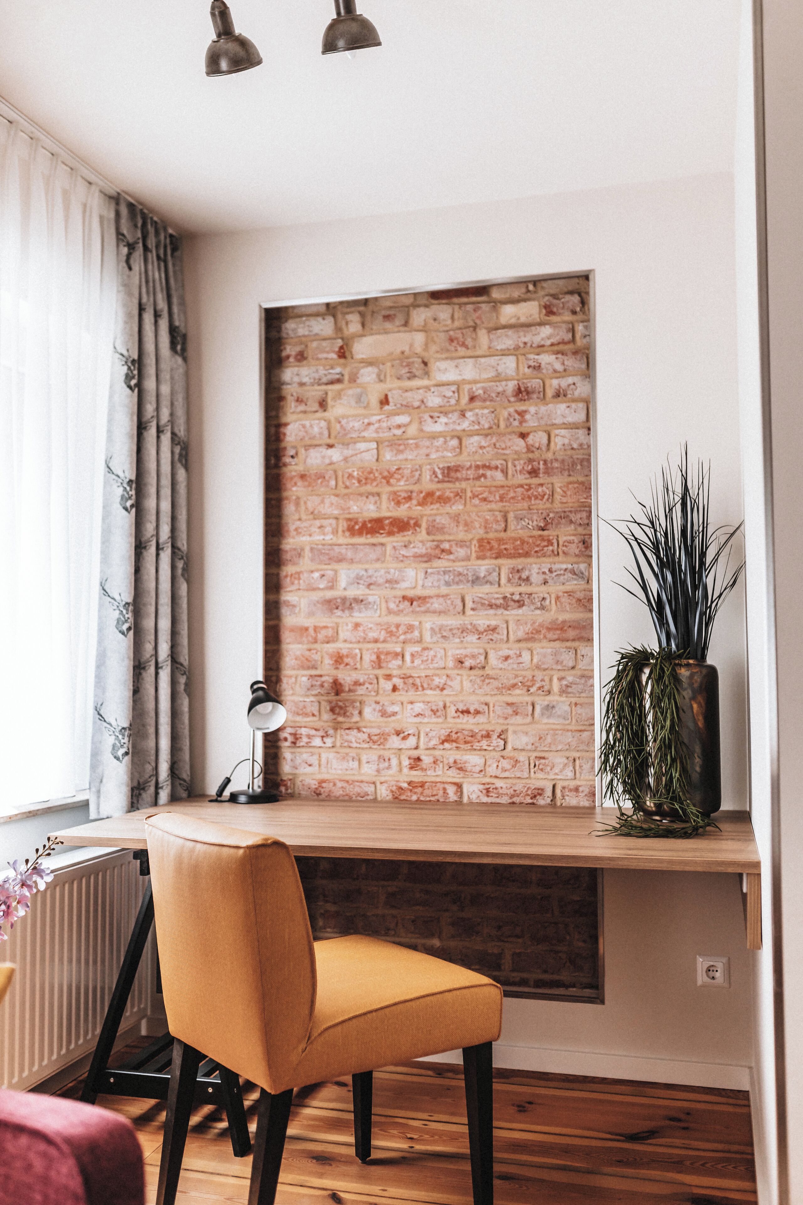 A modern workspace with a brick wall, a wooden desk, a yellow chair, and a potted plant.