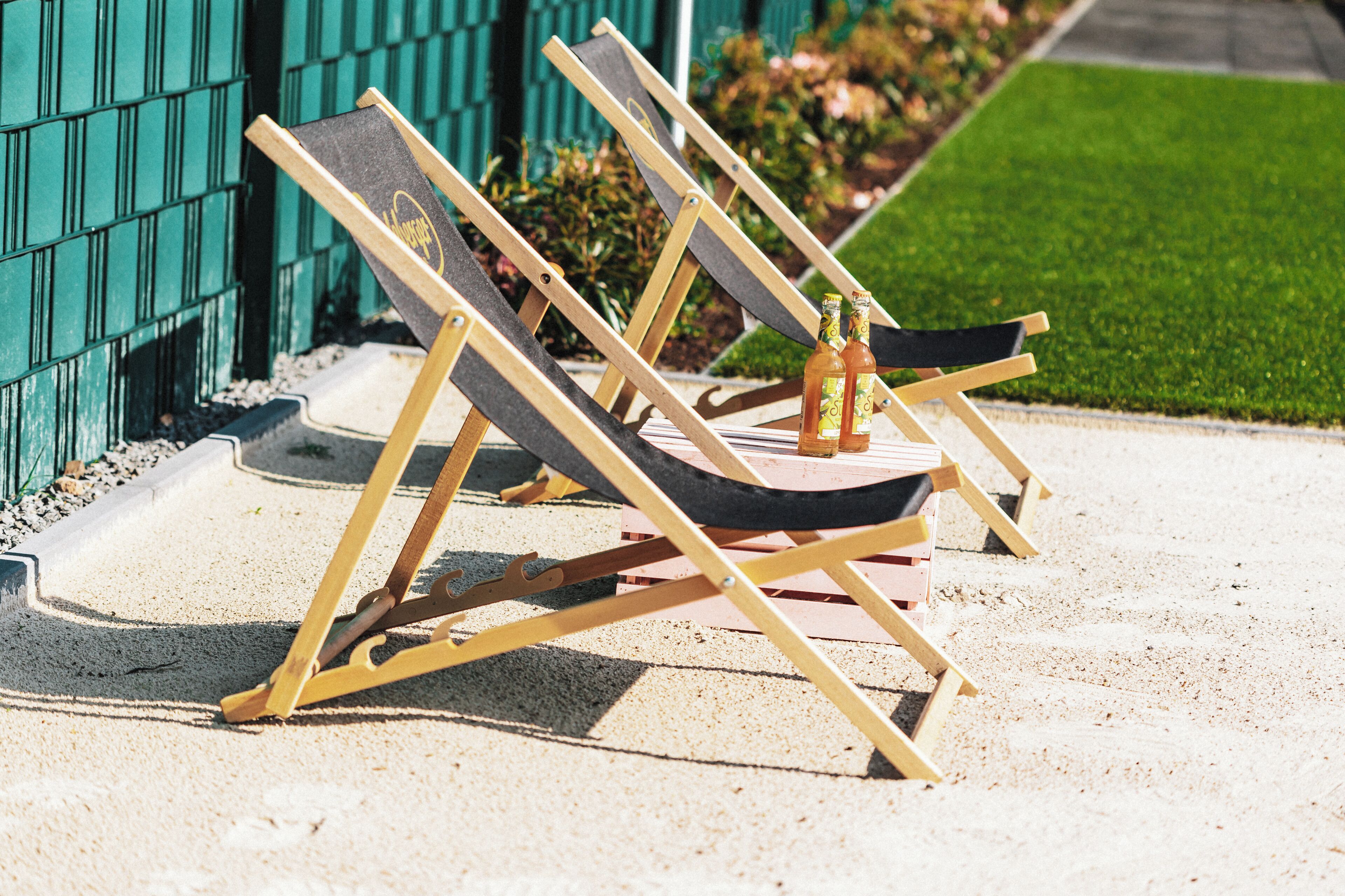 Outdoor lounge chairs arranged on a concrete surface with a green fence and grass in the background.