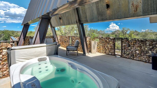 Un jacuzzi en una terraza exterior con una pared de piedra y una estructura de techo metálico.