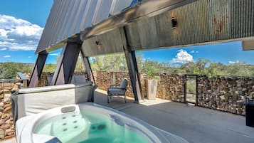 Un jacuzzi en una terraza exterior con una pared de piedra y una estructura de techo metálico.