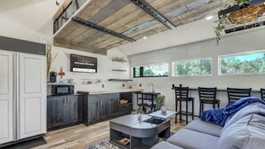 Una cocina moderna con armarios oscuros, un microondas y una mesa de centro. Hay un sofá y una zona de comedor con sillas.